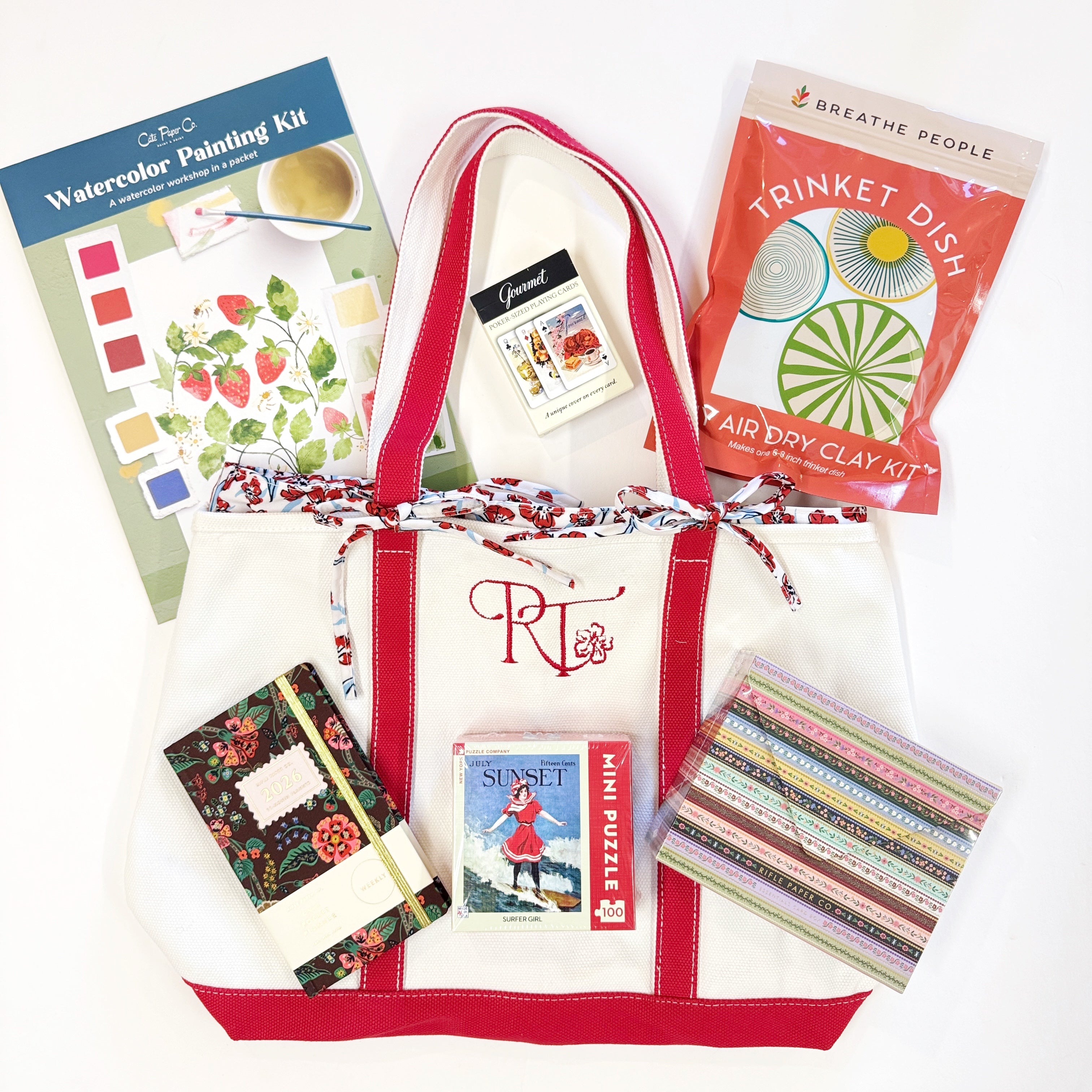 White tote bag with red accents filled with craft items including a watercolor painting kit, air dry clay kit, and other small products.